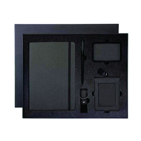 Top view of a dark five-piece executive gift set containing an A5 notebook, metal pen, magnetic card holder, USB keychain and retractable ID cardholder.