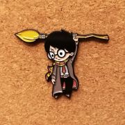 Colourful cartoon wizard enamel pin holding a flying broom against a natural cork background.