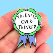 Colourful award-ribbon enamel pin displaying the words Talented Over-Thinker against a blue background.